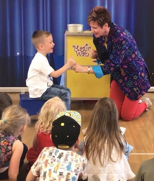 Hampshire based female children's party entertainer Magic Wanda interacting with laughing child helper at his birthday party magic show with other children looking on.